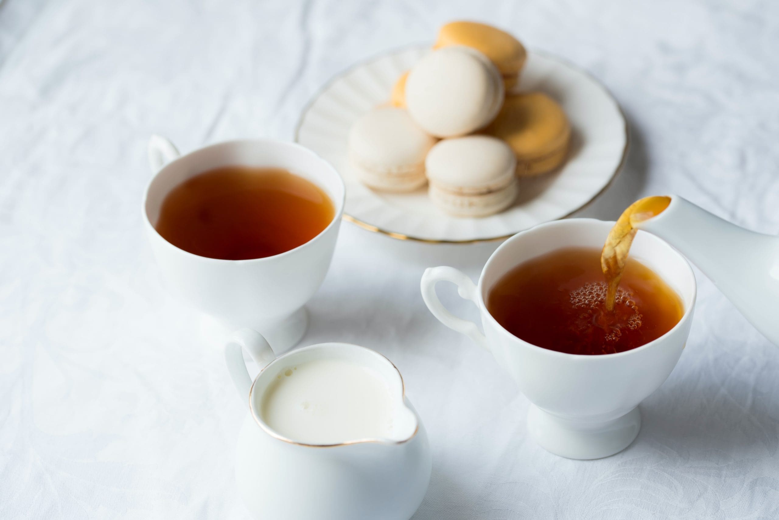 Two cups of tea with creamer and macarons